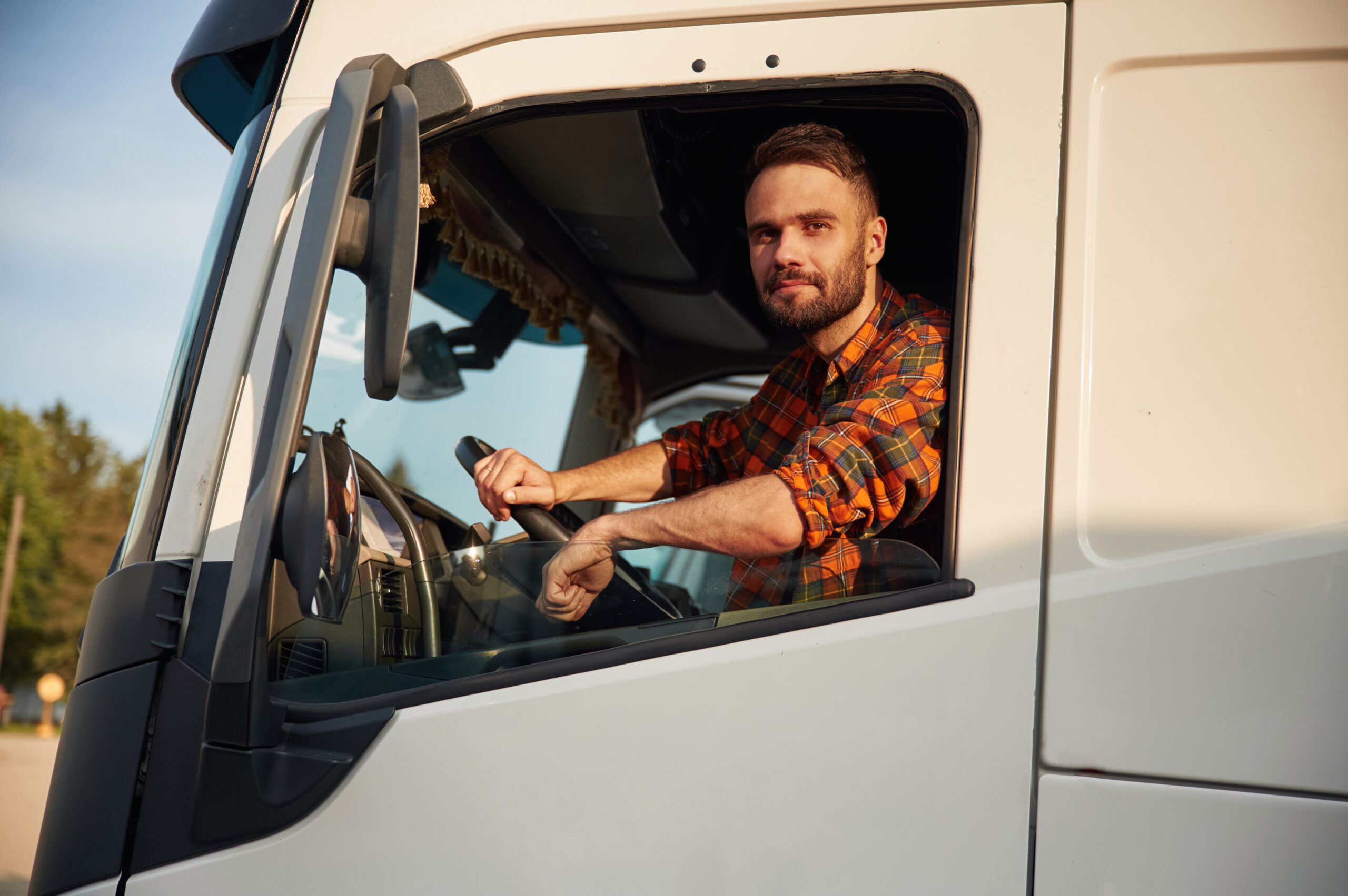 Looking through the door window, sitting inside. Young truck driver in casual clothes