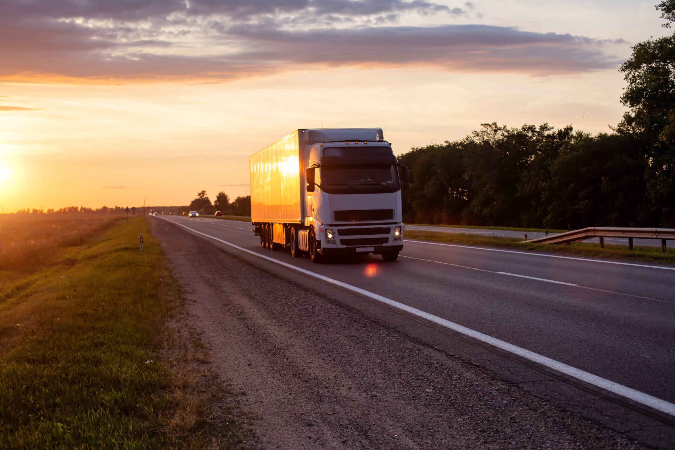 A white truck with a semitrailer transports cargo on the highway in the evening against the backdrop of sunset. Compliance with the rules for the carriage of goods. Transport inspection, european