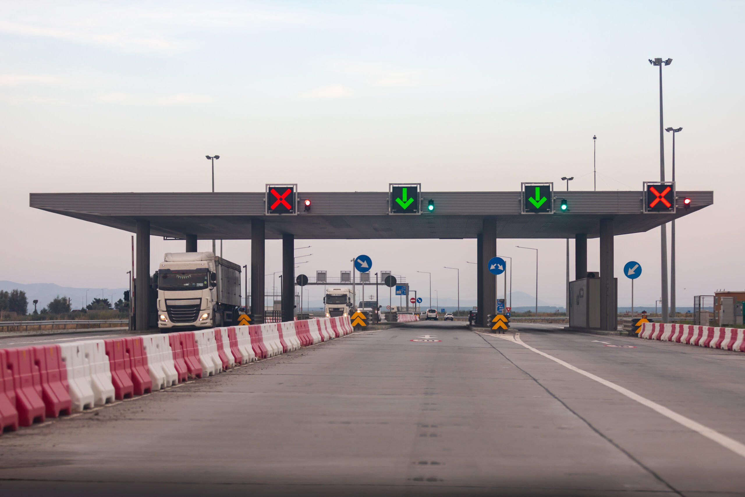 Contemporary highway toll plaza with trucks and illuminated signals under a clear sky, ideal for concepts of transport, infrastructure, and travel.